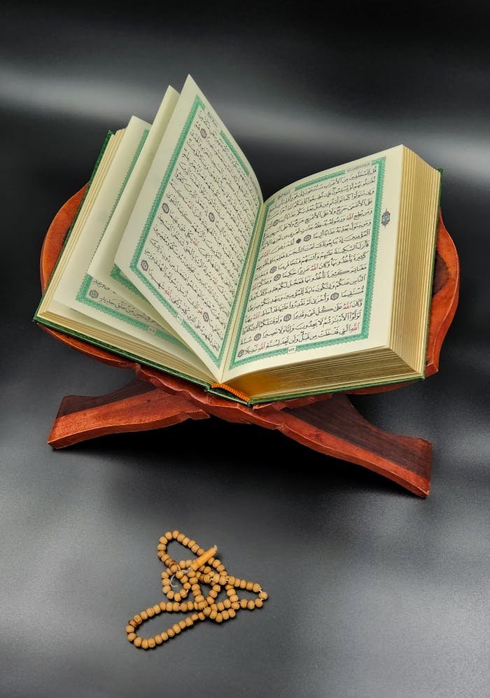 An open Quran displayed on a wooden stand with prayer beads, symbolizing spirituality.