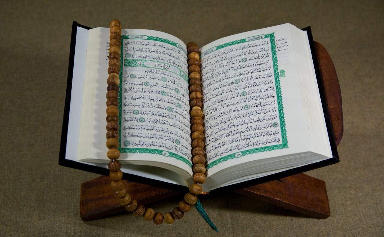 An open Quran with prayer beads displayed on a wooden stand, symbolizing Islamic faith and tradition.